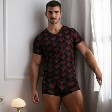 Man wearing a black patterned shirt and matching underwear in a room with white walls and a small table.